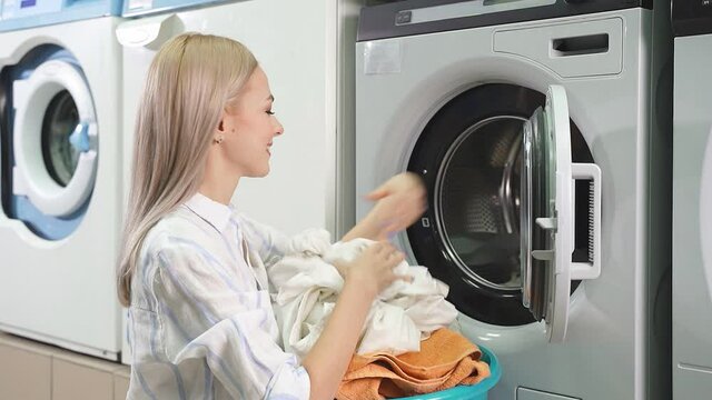 Washing machine washes dirty laundry, woman takes clean laundry out of washing machine, public self-service laundry. slow-motion