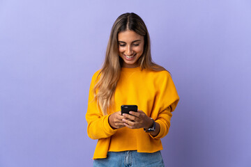 Young hispanic woman over isolated purple background sending a message with the mobile