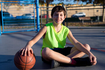 Young basketball player sitting on the court wearing a yellow sleeveless