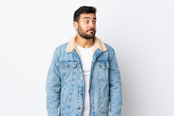 Young handsome man with beard isolated on white background making doubts gesture looking side