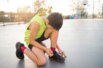 Teenager with basketball, tying shoes at street basketball court