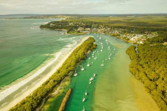 Aerial view of a small boats fleet sailing the Currambene creek at sunset, Huskisson, New South Wales, Australia.