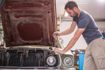 Young caucasian male is seen wrenching an engine or engine bay of an old vintage car. Tune up or...