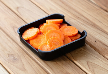fresh raw carrots sliced on square plate isolated on wooden background, shabu, hot pot ingredients