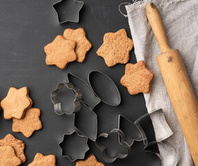 baked star shaped gingerbread cookies, wooden rolling pin and metal cutters on a black table