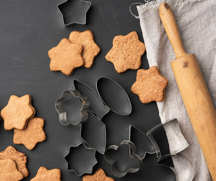 baked star shaped gingerbread cookies, wooden rolling pin and metal cutters on a black table - Powered by Adobe