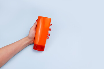 Unbranded orange shampoo and conditioner bottle for branding and label and female hand on blue background. Minimalism, mock-up