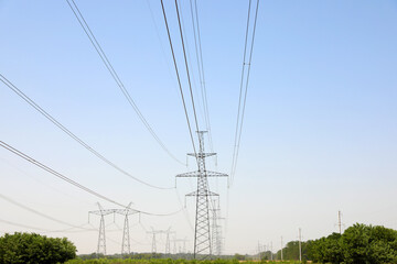 High voltage towers with electricity transmission power lines in field on sunny day