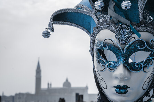 Venice, Italy. Mask in St Mark's Square square (with view on San Giorgio Maggiore island) during Carnival. Moody retro photo.