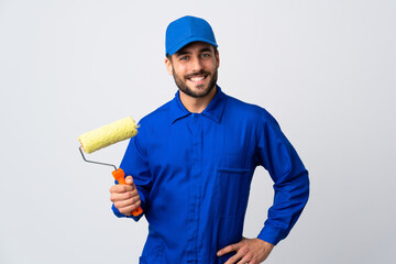 Painter man holding a paint roller isolated on white background posing with arms at hip and smiling