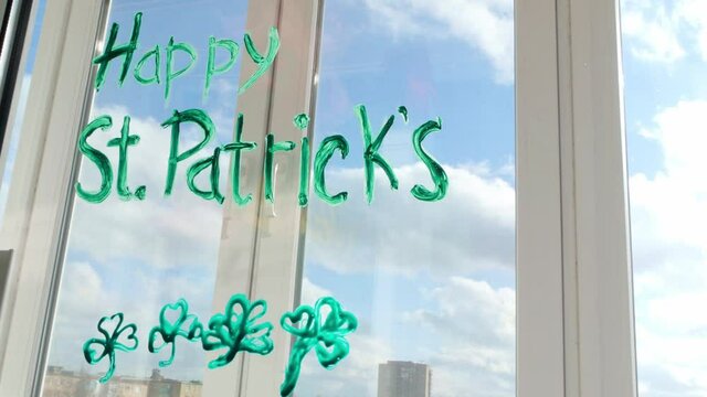 Drawing St. Patrick's Day Man painting green three-leaved shamrocks indoor, festive home decoration, quarantine family leisure. Father draws clover leaves on window glass. Stay home concept New normal