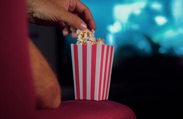 Eating popcorn while watching a movie on the couch at home. Scene in a house with bright lights, a...