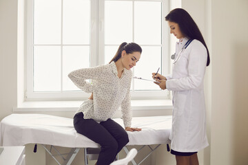 Unhappy young woman complaining about backache sitting on examination bed during visit to doctor's...