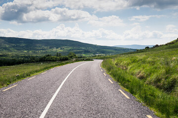 A remote and empty country side Irish road in county Kerry, with green fields and distant mountains in the background
