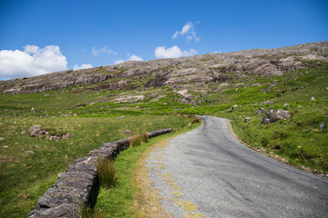 Fototapeta premium A remote and empty country side Irish road in county Kerry, with green fields and distant mountains in the background