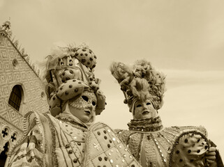 Two noble masks with Doge's Palace at background. St Mark's Square during traditional Carnival in Venice, Italy. Sepia historic photo.