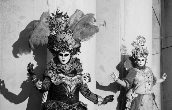 Two masks  in St Mark's Square during traditional Carnival. Black white historic photo.