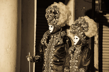 Noble couple masks at St Mark's Square during traditional Carnival. Venice, Italy. Sepia historic photo