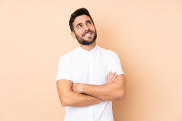 Caucasian handsome man isolated on beige background looking up while smiling