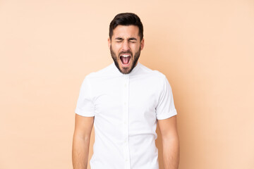 Caucasian handsome man isolated on beige background shouting to the front with mouth wide open