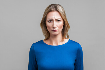 Portrait of unhappy young woman in tight blue clothes looking at camera with gloomy face, frowning...