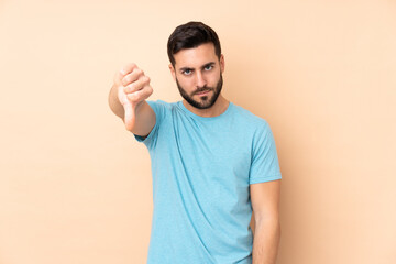 Caucasian handsome man isolated on beige background showing thumb down with negative expression © luismolinero
