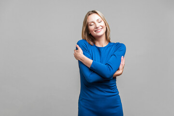 I love myself. Portrait of satisfied selfish woman in elegant tight blue dress embracing herself,...
