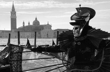 A mask in red in St Mark's Square embankment near the gondolas during the Carnival in Venice, Italy. Black white historic photo.