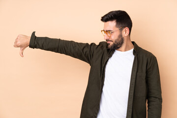 Caucasian handsome man isolated on beige background showing thumb down with negative expression