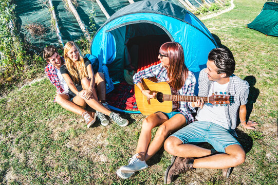 Friends group having fun outdoor singing at picnic camp with vintage guitar - Young people enjoying summer time together at countryside party - Youth travel friendship concept - Vivid bright filter