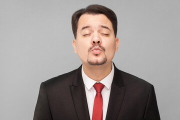 Concept of love. Amorous man kissing an imaginary girl getting ready for a date. indoor studio shot, isolated on gray background. businessman with black suit, red tie and mustache looking at camera.