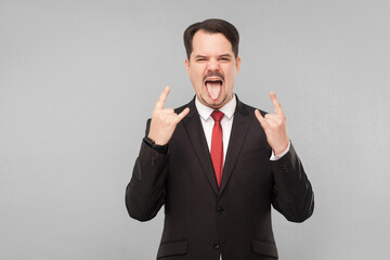 Emotional businessman showing rock sign. indoor studio shot. isolated on gray background. handsome businessman with black suit, red tie and mustache looking at camera.