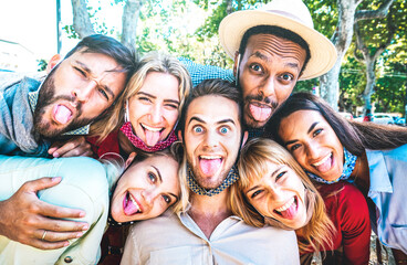 Multicultural friends taking crazy selfie sticking out tongue during Covid 19 third wave - New normal lifestyle concept with young milenial people having fun together - Bright azure sunshine filter