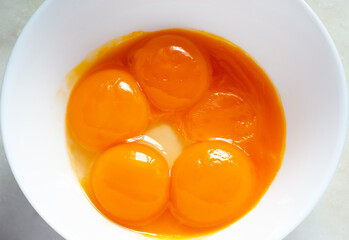 Five raw egg yolks on the plate, one scattered.