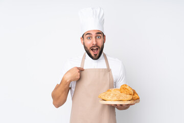 Male baker holding a table with several breads isolated on white background with surprise facial...