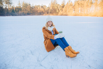 woman sitting in the snow. Woman is having fun outside in the snow. Woman with brown coat on a...