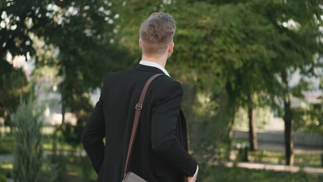 A back view of a young businessman is walking in the park