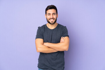 Caucasian handsome man keeping the arms crossed in frontal position over isolated purple background