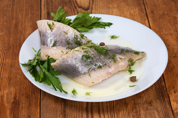 Pickled herring fillets with greens on dish on rustic table