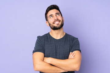 Caucasian handsome man looking up while smiling over isolated purple background