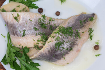 Pickled herring fillets with greens on dish, fragment close-up