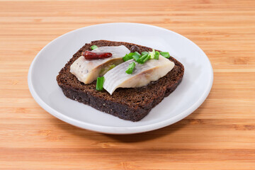Open sandwich with pickled herring slices on brown bread, closeup