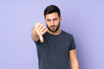 Caucasian handsome man showing thumb down with negative expression over isolated purple background