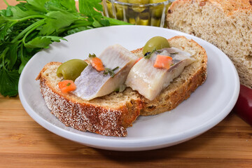 Open sandwich with pickled herring slices and olives, close-up