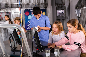 Cheerful interested tweens trying to get out of closed space of escape room stylized under nuclear bunker, using computer