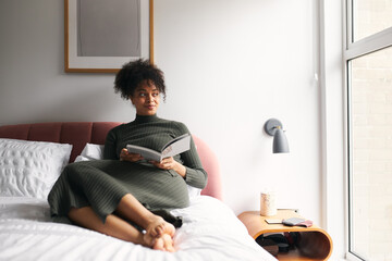 Young Woman Lying And Relaxing On Bed At Home Reading Book