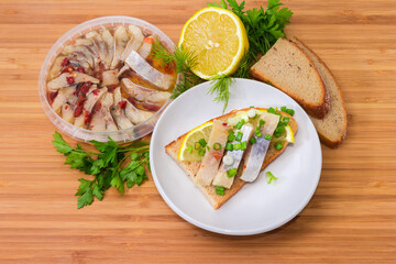 Open sandwich with pickled herring slices among ingredients on wooden surface