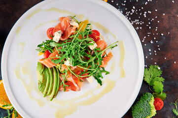 Salad with arugula, salmon, avocado, cherry tomatoes and feta cheese on a white plate. Oxidized background. close-up