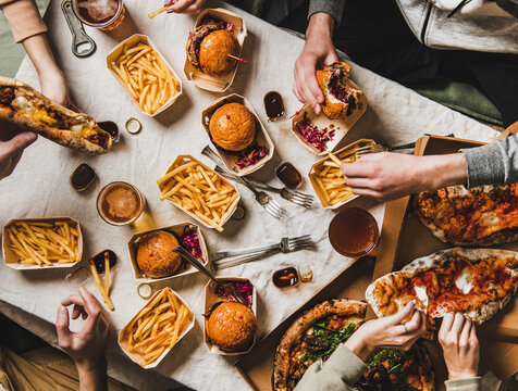 Lockdown Family Fast Food Dinner From Delivery Service. Flat-lay Of Friends Group Eating Burgers, Fries, Sandwiches, Pizza, Drinking Beer At Home Party Over Table Background, Top View