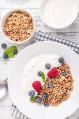 Homemade granola with yogurt and fresh berries in white ceramic plate on wooden background. Vertical photo - Image
